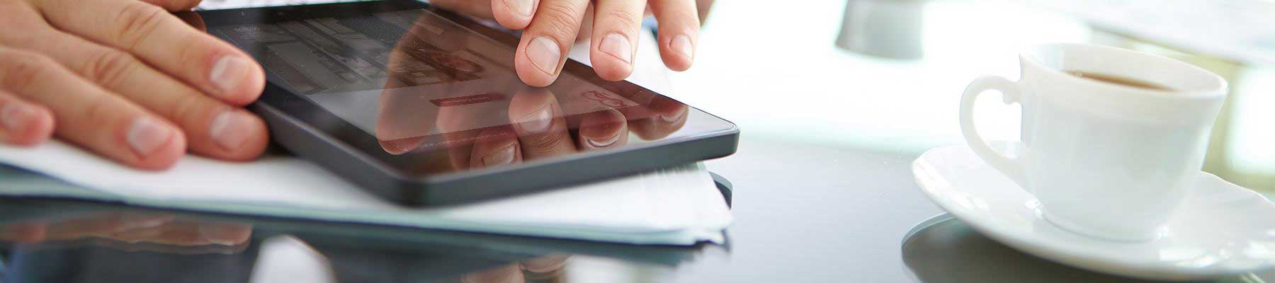 close up of hands using a smart device beside a cup of coffee