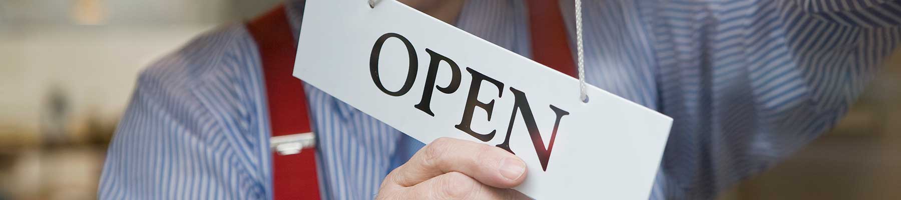 man in striped shirt and apron turning a store sign out to show the store is now open