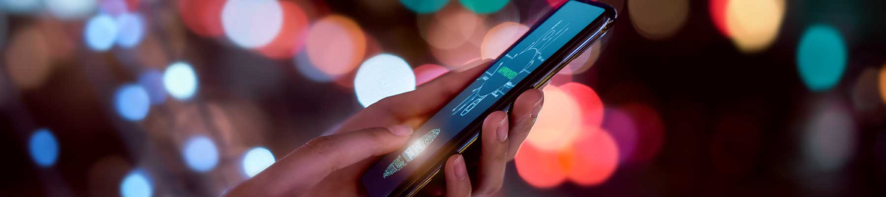 Close-up of hands scanning fingerprint on smartphone to unlock mobile phone on bokeh colors light in night atmospheric city